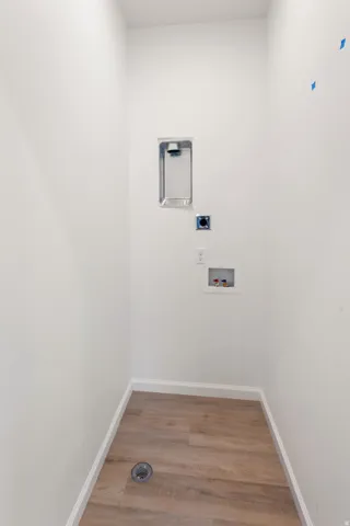 Dedicated laundry area featuring wood-finish flooring, white walls, and a floor drain