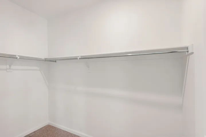 Walk-in closet featuring white walls, white shelving, and a metal hanging rod system