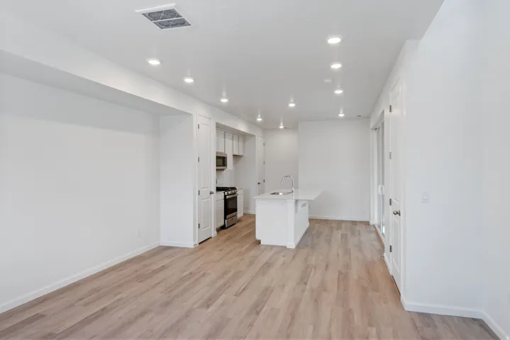 Open-concept living area featuring light wood-finish flooring, recessed lighting, and crisp white walls