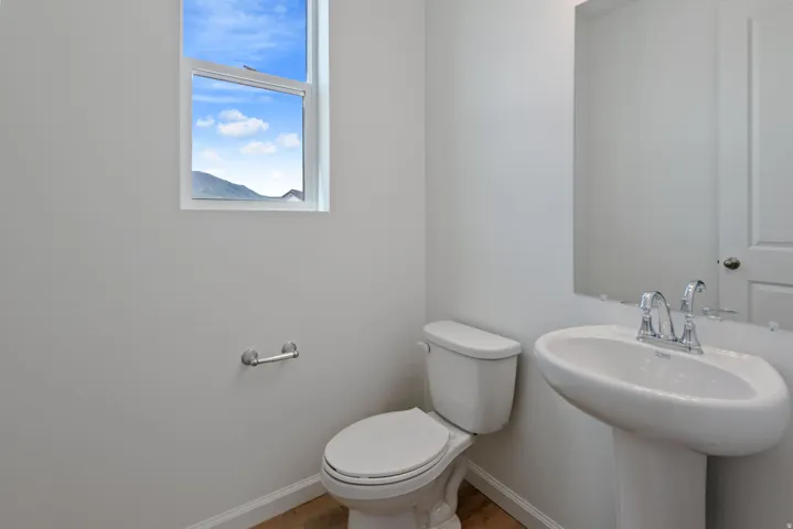 Powder room featuring a pedestal sink with chrome faucet, a white toilet, and a window with a mountain backdrop