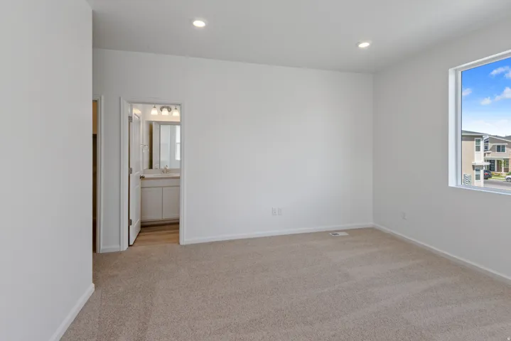 Spacious carpeted room featuring a large window, recessed lighting, and a doorway opening to a bathroom with a vanity and mirror