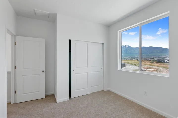 Carpeted room featuring a large window with mountain scenery, dual-panel sliding closet doors, a single interior door, and neutral wall tones