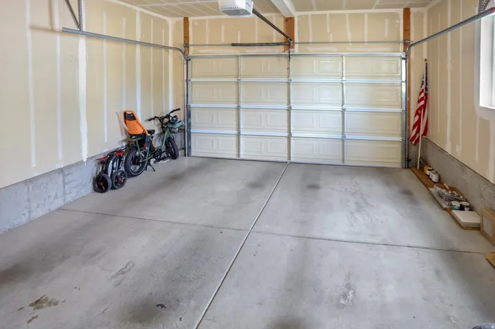 Spacious garage featuring a sectional overhead door, exposed wood studs, concrete flooring, and a large window providing natural light