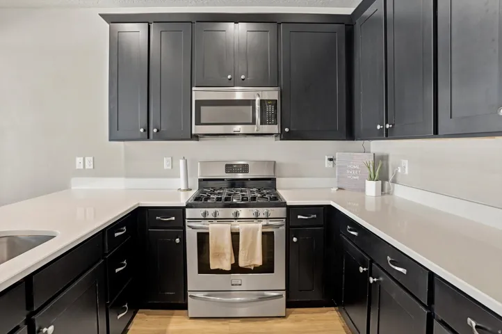 U-shaped kitchen featuring dark cabinetry, light countertops, stainless steel appliances, and wood-finish flooring