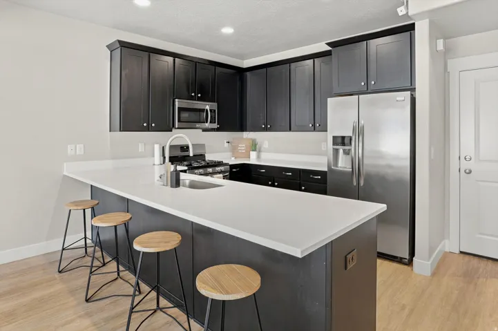 Modern kitchen featuring dark cabinetry, stainless steel appliances, a center island with a light-toned countertop, a gas range, and wood-finish flooring
