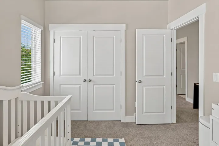 Carpeted room with a double-pane window featuring white blinds, double panel closet doors with round knobs, and a single panel interior door with a round knob