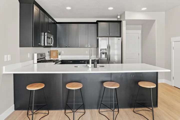Contemporary kitchen featuring dark cabinetry, stainless steel appliances, light countertops, a built-in kitchen island, and recessed lighting