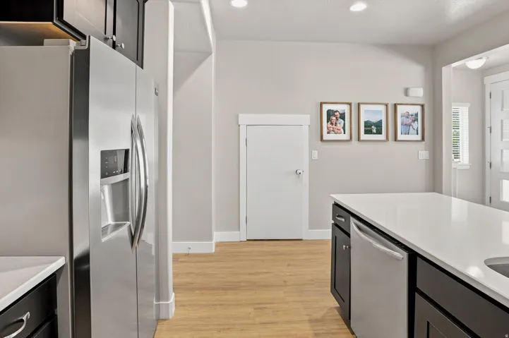 Kitchen featuring a stainless steel side-by-side refrigerator, dark cabinetry, light countertops, wood-finish flooring, and recessed lighting