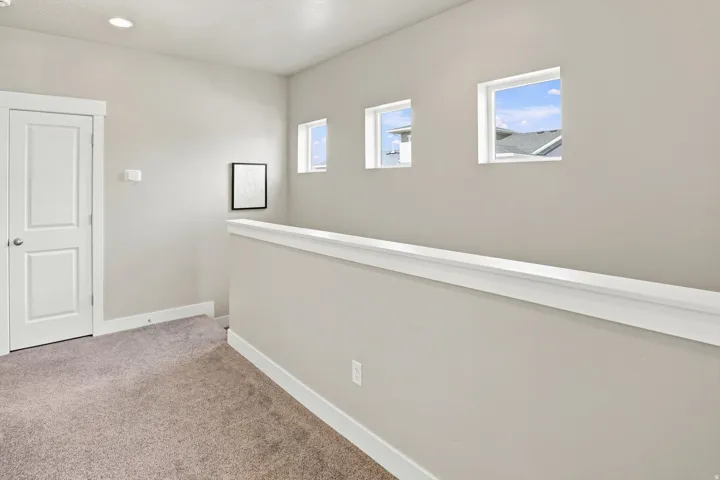 Carpeted loft area featuring a white railing, three square windows, recessed lighting, and a paneled door
