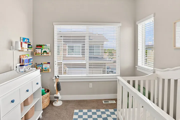Neutral-toned walls and carpeted flooring define this room, featuring two windows with white horizontal blinds