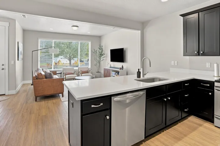 Kitchen with dark cabinetry and light countertops, featuring an integrated stainless steel sink and a stainless steel dishwasher