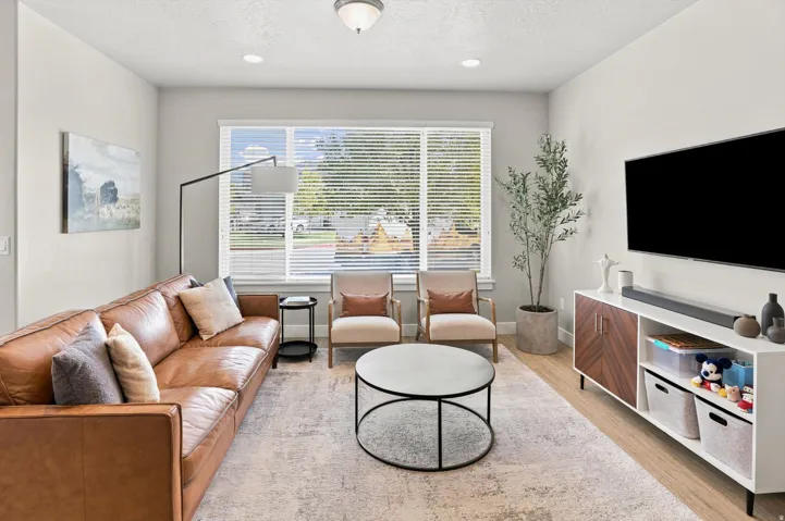 Spacious living area featuring light-toned walls, wood-finish flooring, and a large window with blinds