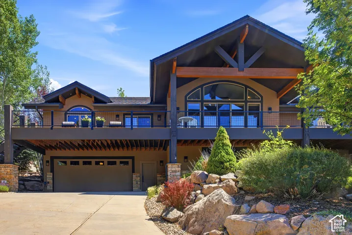 Modern exterior featuring multiple balconies with metal railings, a prominent arched window, exposed wooden beams, and an integrated multi-car garage with a single door