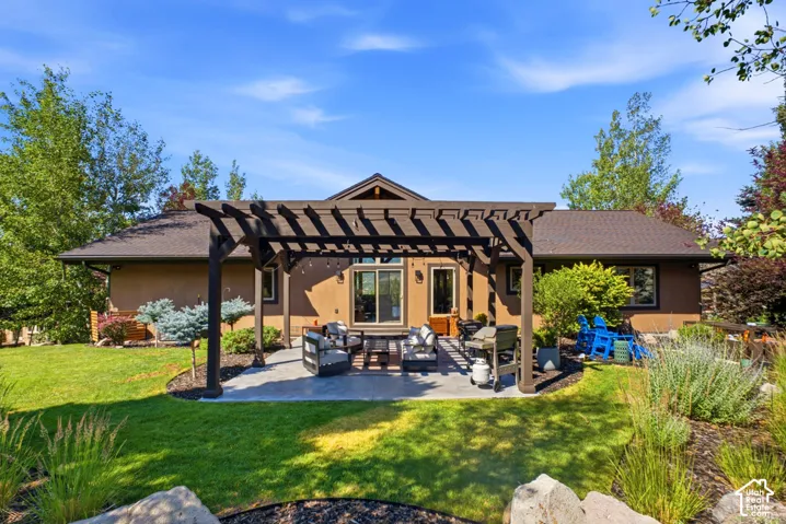 Expansive backyard featuring a stone patio, a dark wood pergola, and a lush green lawn