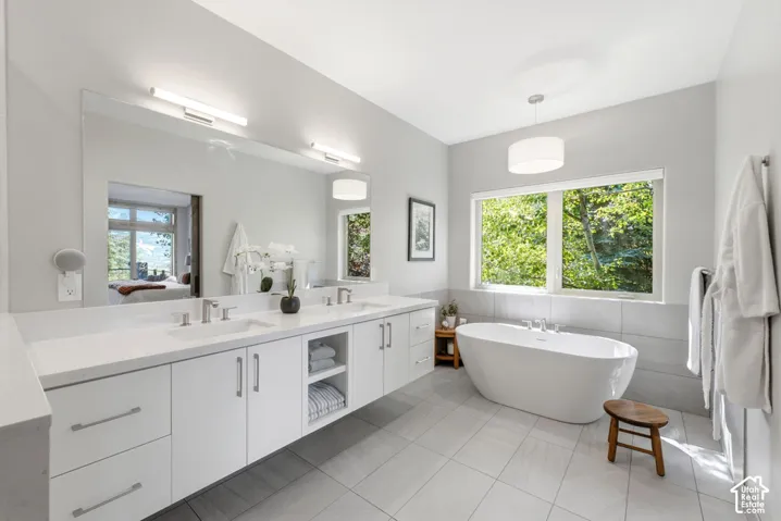 Spacious bathroom featuring a freestanding soaking tub, dual vanity with white cabinetry, large vanity mirror, and light-toned tile flooring