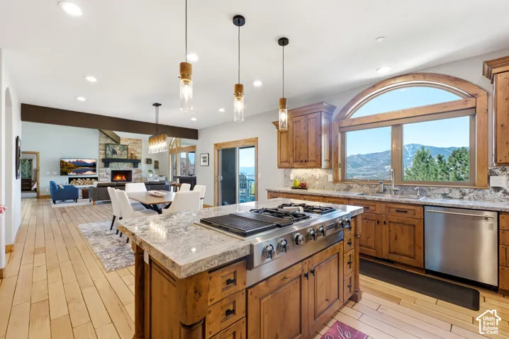 Open-concept kitchen featuring an oversized island with a built-in range, wood-finish cabinetry, granite countertops, and a large arched window