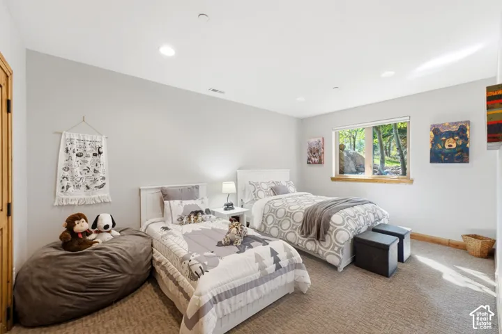 Spacious bedroom featuring light neutral wall paint, recessed lighting, a wood-trimmed window with exterior tree views, and wall-to-wall carpeting