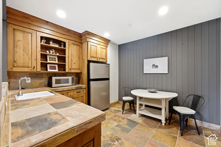 Wet bar featuring rich wood cabinetry, integrated shelving, and a stainless steel refrigerator