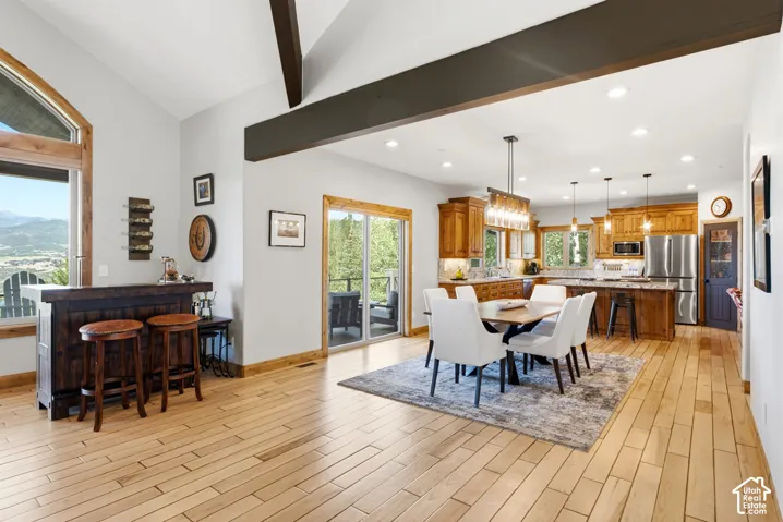 Spacious open-concept living area featuring light wood-finish flooring, vaulted ceilings with exposed beams, a built-in bar, and a kitchen with wood cabinetry and an island