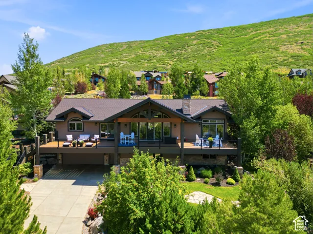 Contemporary mountain home featuring a spacious exterior deck, stone accents, mature landscaping, and a multi-car driveway