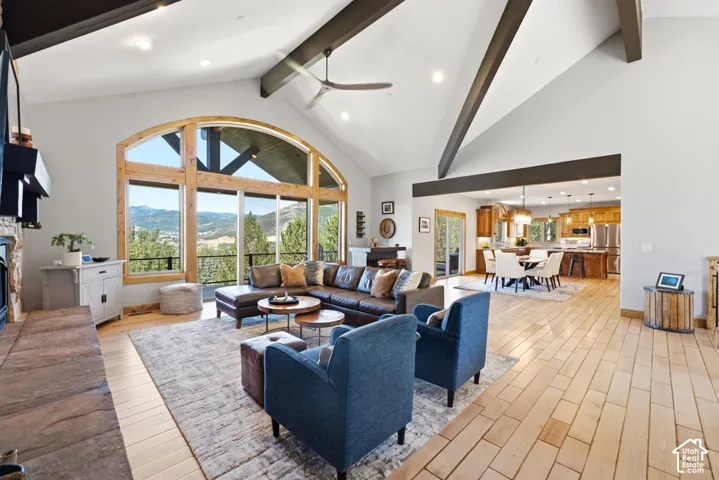 Vaulted ceiling living area with exposed beams, featuring a stone fireplace, light wood-finish flooring, and a large arched window with mountain scenery