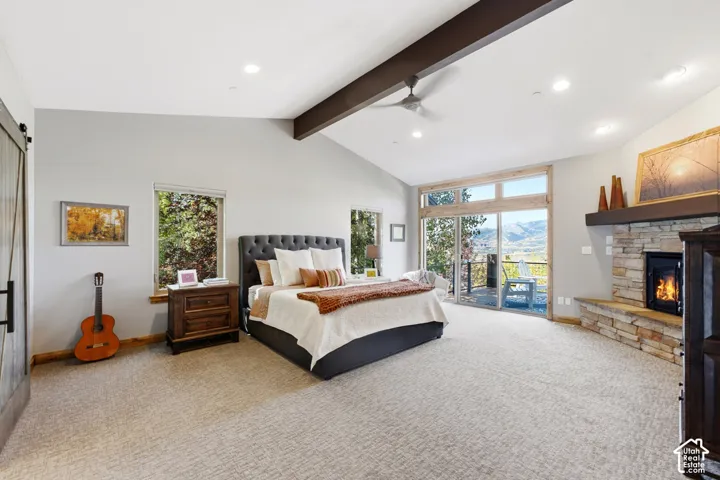 Spacious room featuring vaulted ceilings with exposed beams, a built-in stone fireplace, and a sliding glass door opening to an outdoor area