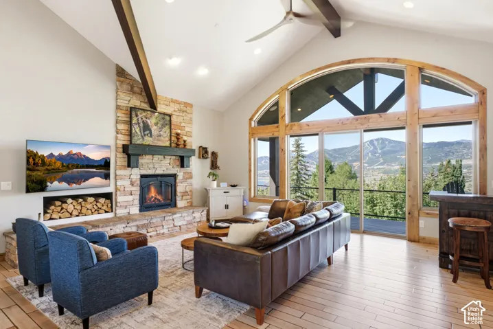 Vaulted ceilings featuring exposed timber beams, a stone fireplace with hearth, and an expansive arched window framing mountain scenery