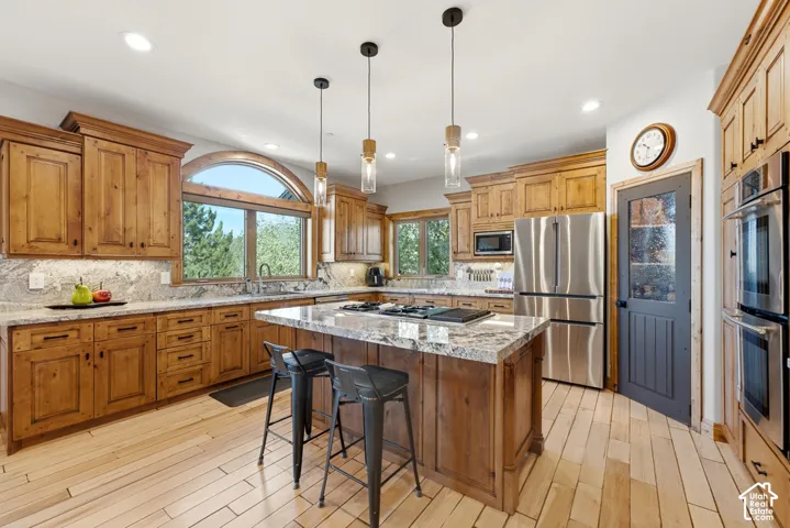 Open-concept kitchen featuring wood-finish cabinetry, light-toned wood-finish flooring, and a central island with a cooktop