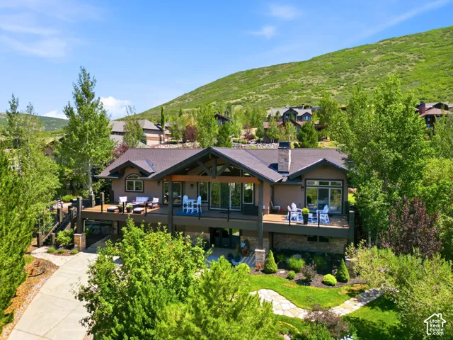 Modern mountain-style residence featuring a dark shingle roof, stone chimney, and an expansive elevated deck