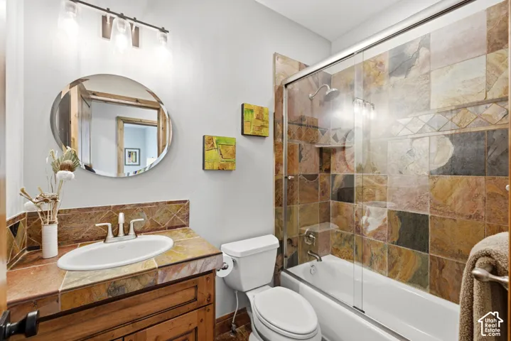 Bathroom featuring natural stone tile shower surround with glass enclosure, coordinating stone countertop, and a wood-finish vanity with an undermount sink