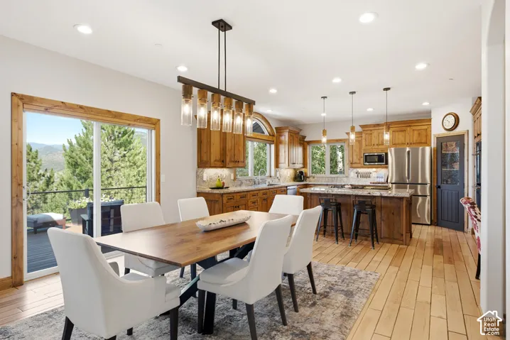 Open-concept dining area featuring a modern linear chandelier, wood-finish flooring, and direct access to an outdoor deck through sliding glass doors
