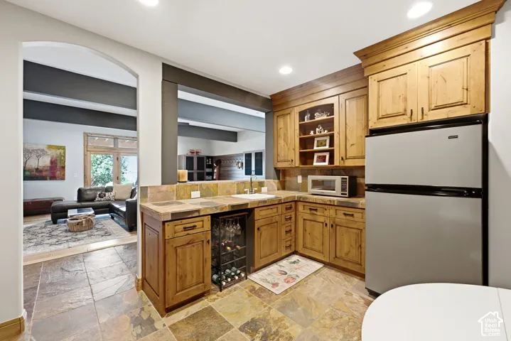 Kitchenette featuring slate floor tile, natural wood cabinetry, stone-finish countertops with a tile backsplash, and a built-in wine rack