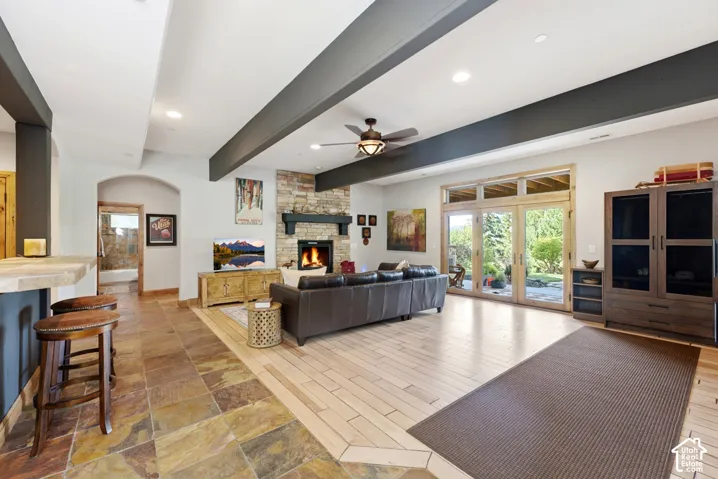 Spacious living area featuring a stone-clad fireplace, wood-finish flooring, and exposed ceiling beams