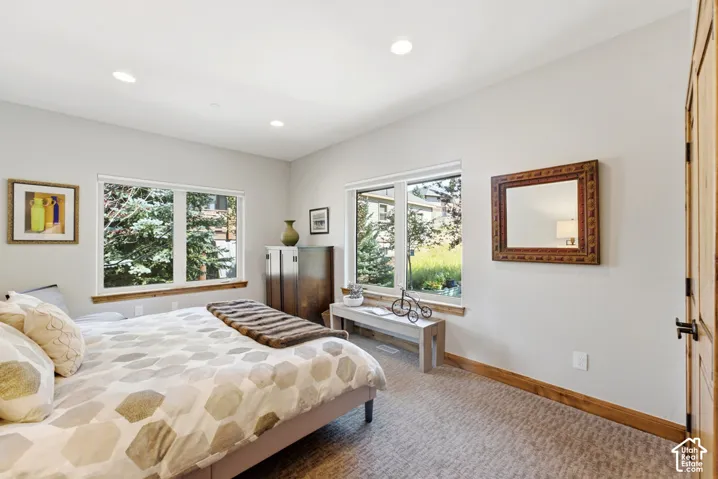 Spacious room featuring multiple windows, recessed ceiling lighting, light-colored walls, wood-finish trim, and carpet flooring