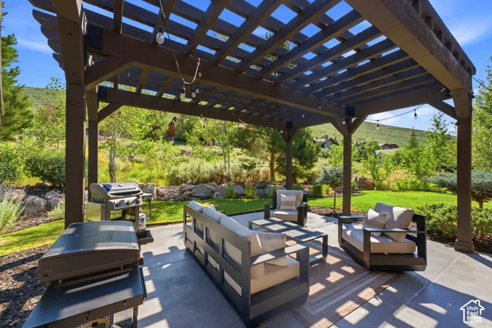 Expansive outdoor patio featuring a large pergola, concrete flooring, and string lighting