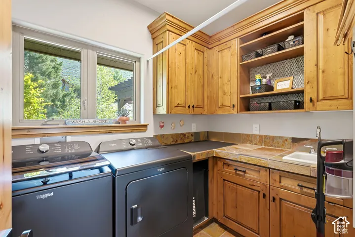 Laundry area featuring wood cabinetry with crown molding, a built-in utility sink, and a tiled countertop