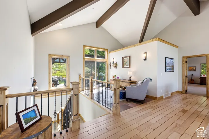 Vaulted ceilings with exposed beams, wood-finish flooring, two large windows with wood trim, wood staircase with wrought iron balusters, and wood-paneled walls