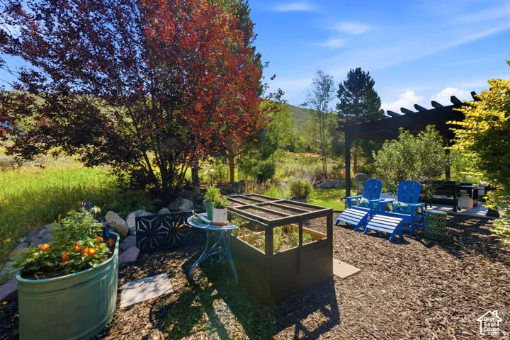 Outdoor living area featuring a dark-stained wood pergola, a raised garden bed, a decorative metal screen, a rock garden, and mature landscaping