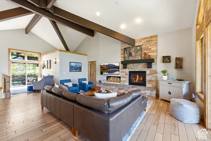 Vaulted ceilings with exposed beams, stone-clad fireplace with mantel, and wood-finish flooring