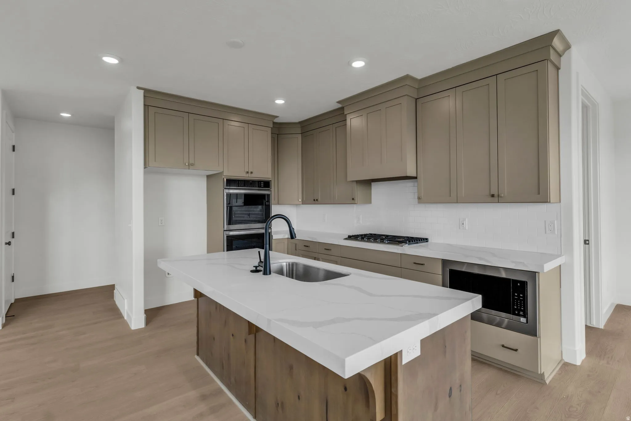Kitchen featuring a central island, undermount sink, quartz countertops, upgraded appliances including double ovens and gas cooktop.