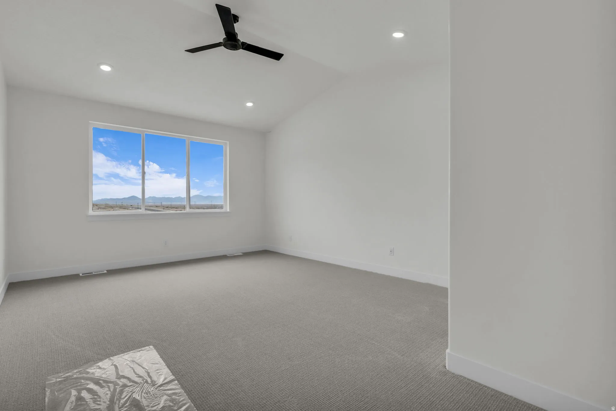 Vaulted  and oversized primary bedroom with beautiful sleek fan and large window.