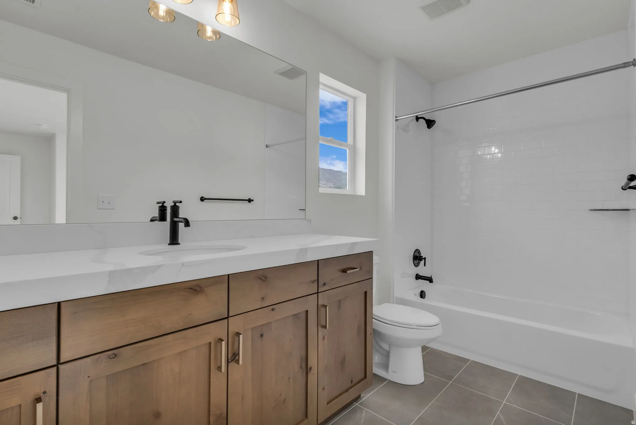 Guest suite full bath featuring custom tiled shower surround, wood cabinetry, matte black fixtures, and beautiful Quartz countertops.