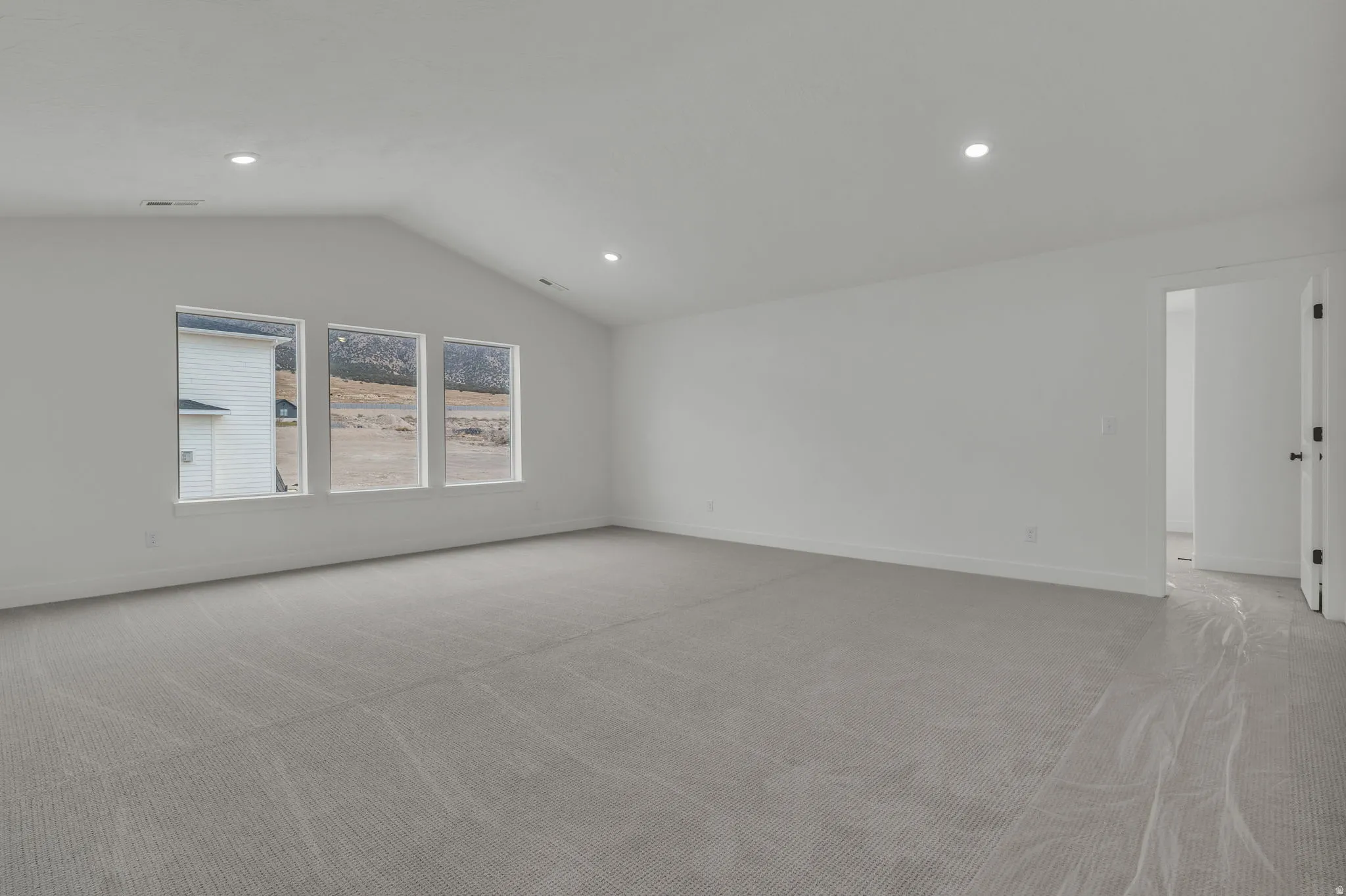 Spacious loft at the top of the stairs featuring vaulted ceilings, three large windows, with bedrooms on either side.