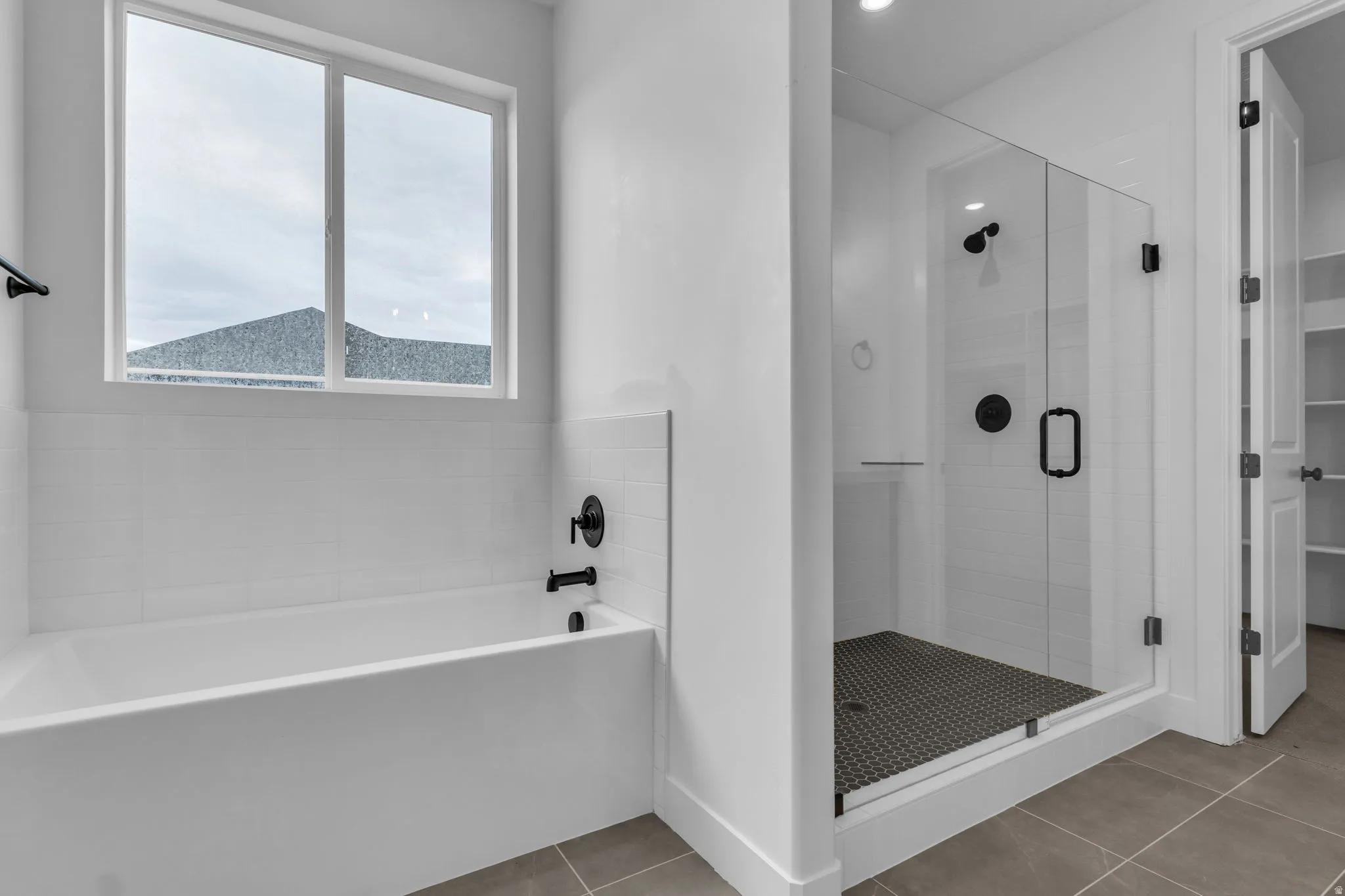 Primary spacious bathroom featuring a built-in soaker tub, a walk-in shower with euro glass, matte black fixtures and custom tile flooring and shower surround.