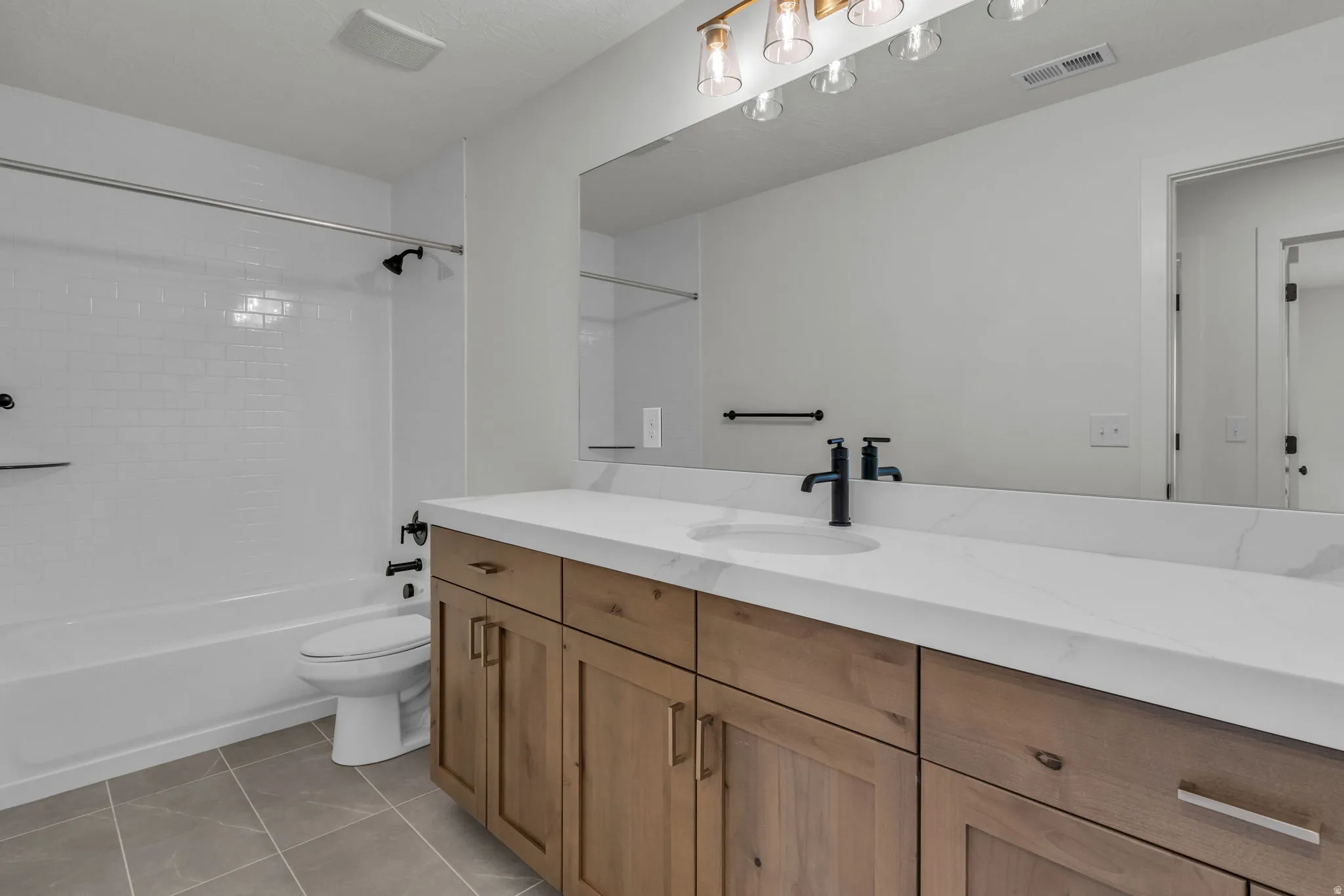 Bathroom featuring custom tiled shower surround, wood cabinetry, matte black fixtures, and beautiful Quartz countertops.