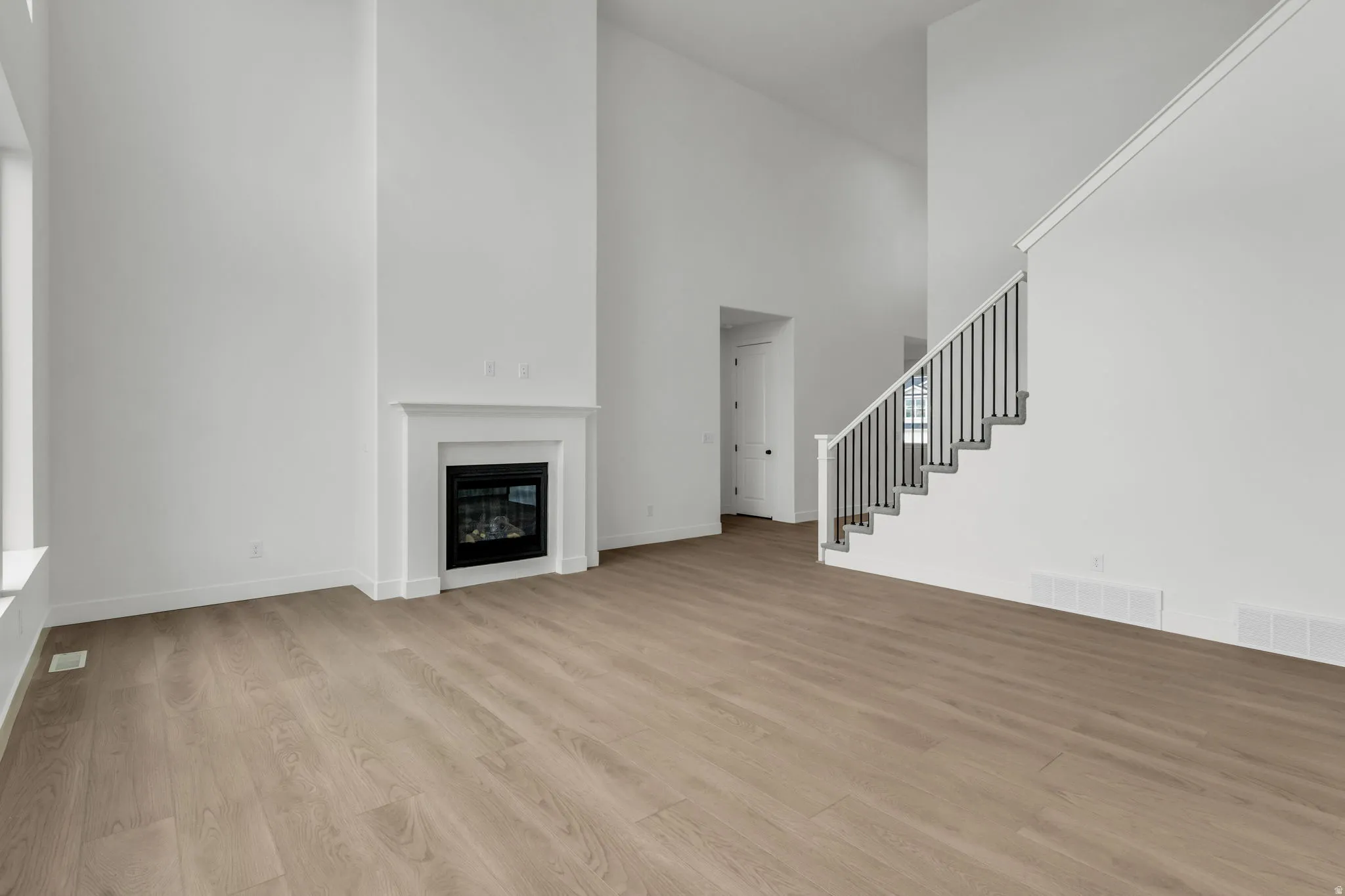 Spacious great room, gas fireplace with white custom mantel, two story ceilings, with open  staircase and railing.