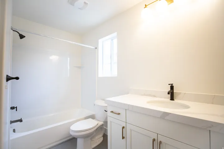 Full secondary bath with painted white wood cabinets and quartz slab countertop.