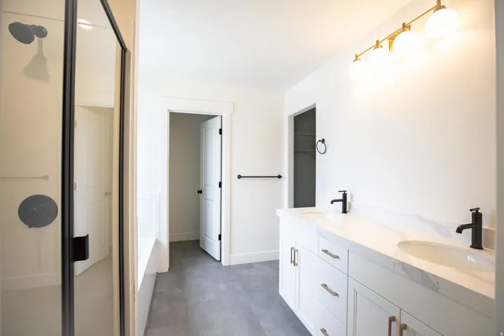 Full primary bath with painted white wood cabinets, quartz slab countertops, large walk-in shower and soaker tub.