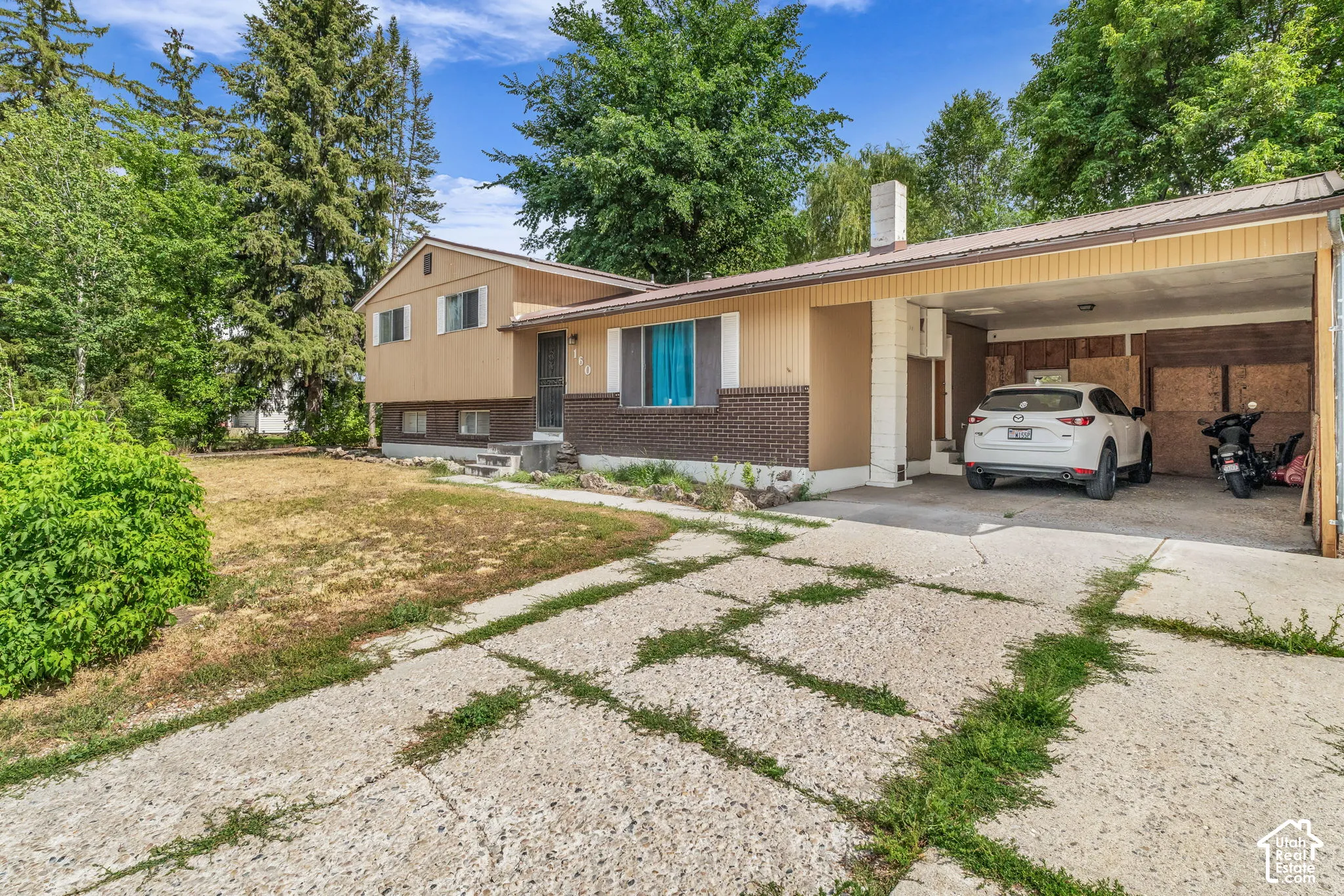 Split-level residence featuring a brick and siding exterior, an integrated carport, mature trees, and a concrete driveway