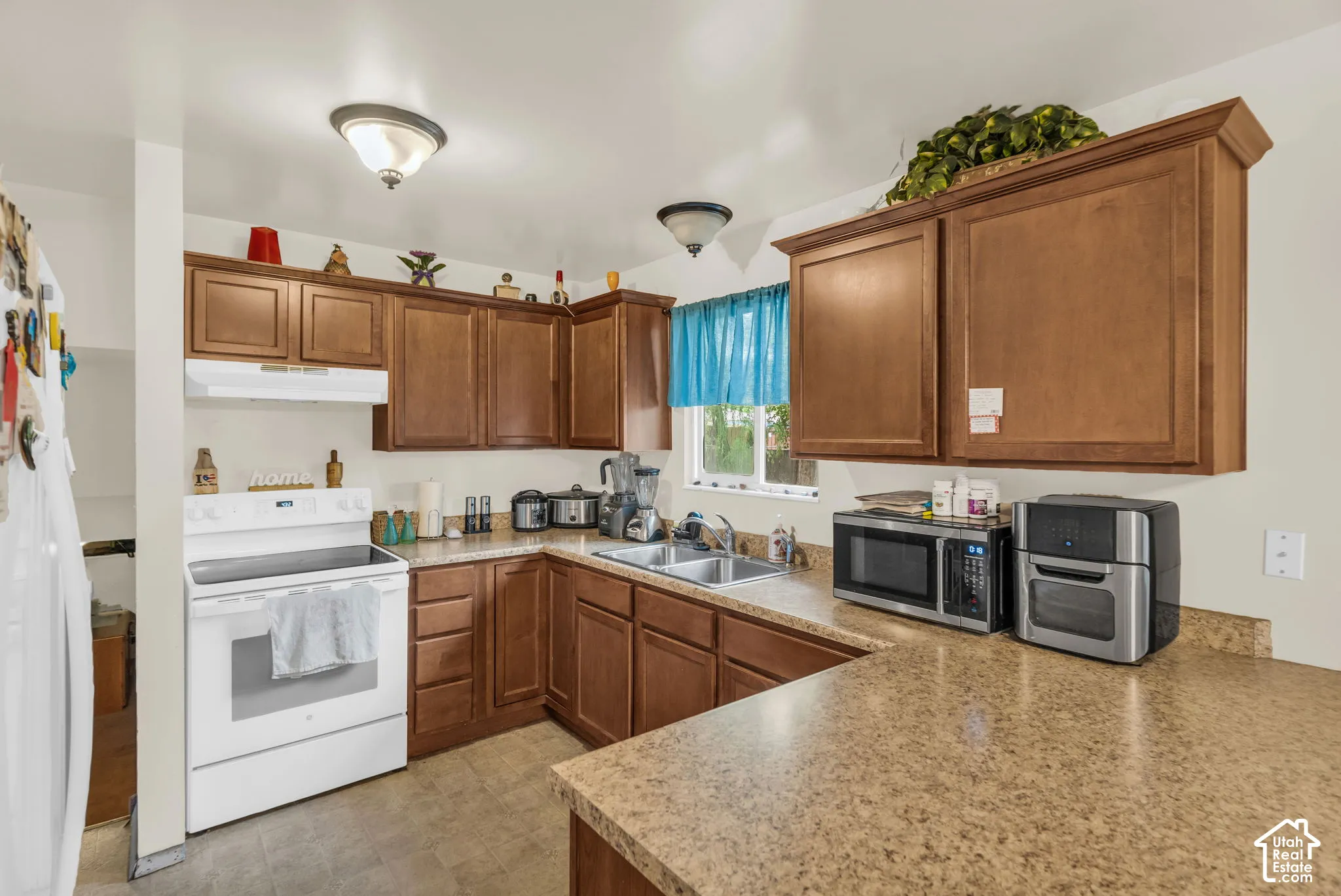 Kitchen featuring wood-finish cabinetry, light-toned countertops, and a double basin sink with a window above